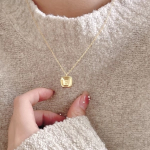 Close-up of golden square pendant with embossed letter S on a minimalist fine chain