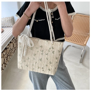Detail of straw tote bag featuring green leaf embroidery and delicate white lace bow