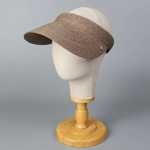Detalle de la visera de rafia marrón con textura tejida y adorno metálico lateral