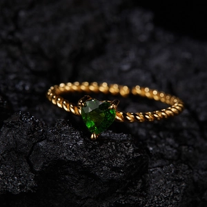 Macro detail of a heart-shaped green gemstone ring on a dark textured rock background