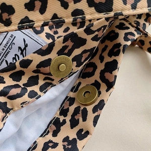 Macro shot of leopard print canvas texture with retro magnetic brass buckle and brand label