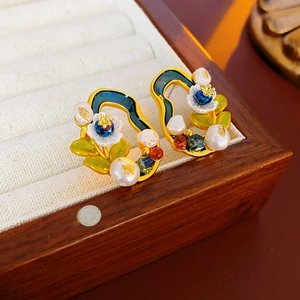 Close-up of vintage flower earrings with pearls and colorful enamel on a wooden box