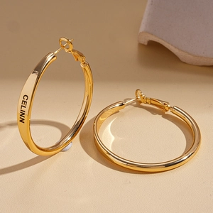 Polished gold round hoop earrings with letter engraving on a neutral textured background