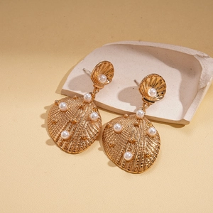 Detail of gold seashell earrings with embedded pearls on a ceramic textured piece