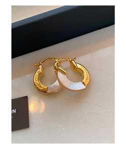 Detailed macro of gold-plated hoop earrings with mother of pearl and Confession engraving