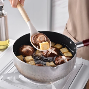 Silicone soup ladle with wooden handle scooping food from a pot in a kitchen setting
