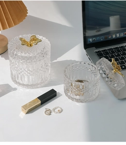 Detail of embossed glass storage jars with elegant gold butterfly lids on a white desk