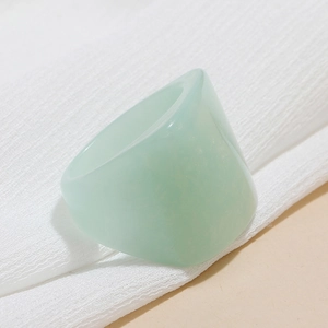 Macro detail of mint green wide resin ring on white textured fabric background