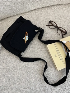 Minimalist black canvas crossbody bag with colorful planet embroidery on textured surface