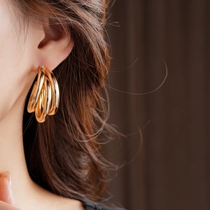 Gros plan de boucles d'oreilles créoles dorées multicouches en forme de C sur l'oreille