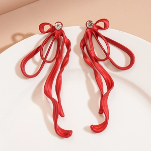 Detail of red matte metal bow earrings with crystal stud on white ceramic tray