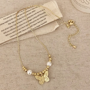 Elegant gold butterfly necklace featuring copper beads and pearls on textured fabric