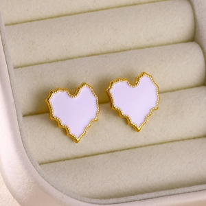 Detailed close-up of heart-shaped gold stud earrings with white enamel in jewelry box