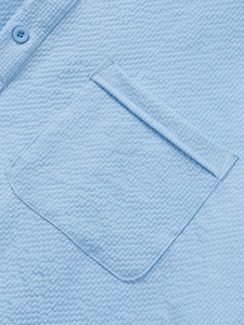 Macro detail of sky blue seersucker shirt featuring a chest pocket and resin button