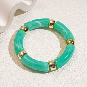 Detail of green marble resin tube beads and golden metal rings on a minimalist white surface