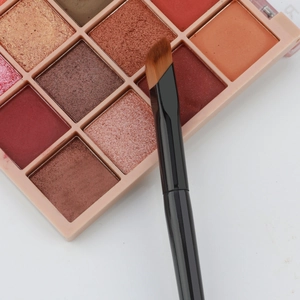 Detailed view of an angled concealer brush with gradient bristles and makeup palette