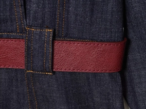 Detailed macro view of a wine red faux leather belt on dark blue denim dress fabric
