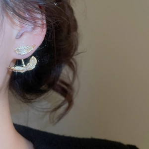 Detailed view of leaf-shaped gold-plated zircon earrings worn on a model's ear lobe
