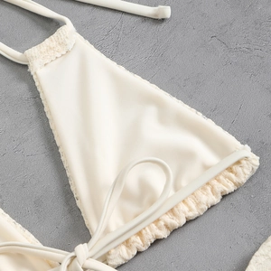 Close-up of white bikini top with wavy lace trim and neck ties on grey stone