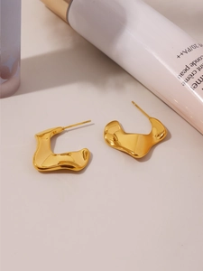 Detailed view of irregular wavy C-shaped gold-plated earrings on a refined surface