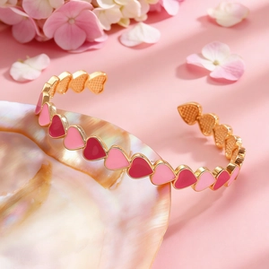 Dettaglio di un bracciale aperto dorato con cuori in smalto rosa su base di conchiglia