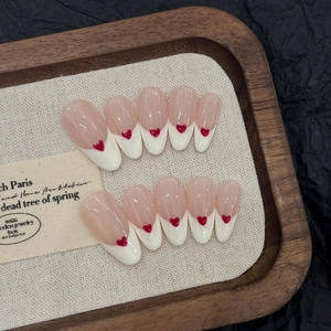Faux ongles French avec cœurs rouges 3D présentés sur un plateau en bois