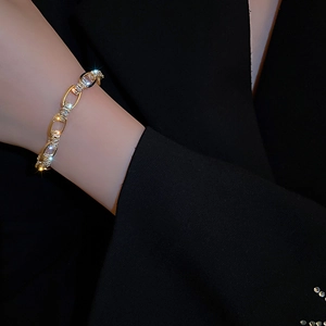 Nahaufnahme eines goldenen Zirkonia-Kettenarmbands mit funkelnden Kristallen auf schwarzem Ärmel