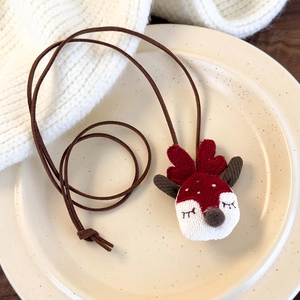 Detail view of cute reindeer plush necklace pendant on a beige ceramic plate