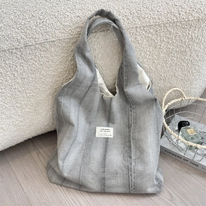 Detailed close-up of grey tie-dye canvas tote bag with woven label on wooden floor