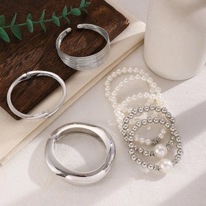 Detail of stacked silver-colored bracelets with oversized pearls on a wooden tray