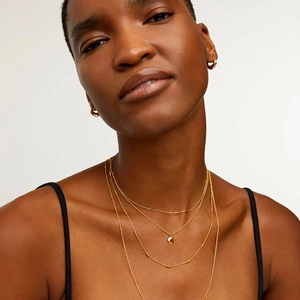 Close-up of layered 18K gold necklaces and matching hoop earrings on model