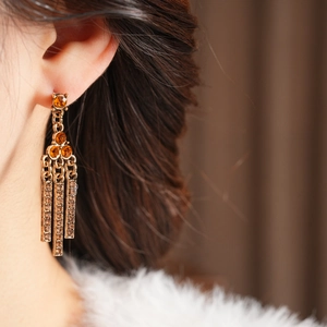Detail of vintage gold drop earrings with amber stones and tassels on a model