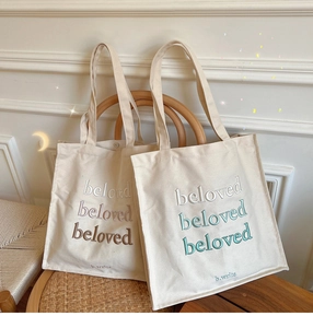 Detailed embroidery of the beloved text on canvas tote bags in brown and green gradients