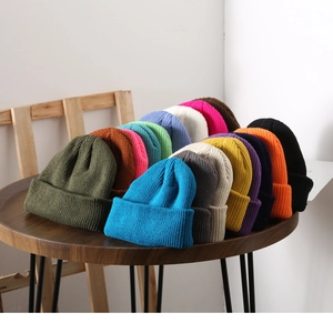 Close-up of colorful knitted beanies neatly stacked on a wooden table in many shades