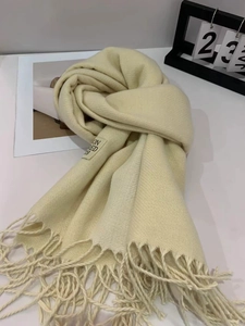 Detail of cream white knit scarf featuring long fringe tassels and a minimalist woven label