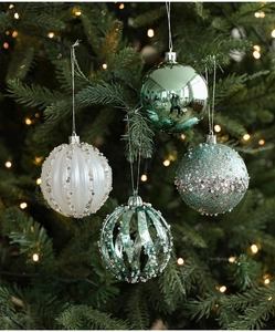 Close-up of green and white 8cm Christmas ornaments hanging on a tree with festive lights