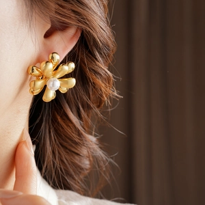 Detail of 18k gold-plated flower earring with pearl center worn by a female model