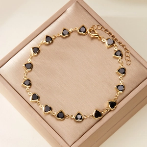 Detail of golden bracelet featuring black heart gems on a beige display box