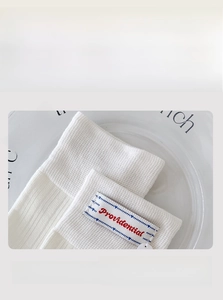 Detail of white knit crew socks featuring red embroidered label and elastic non-slip cuffs
