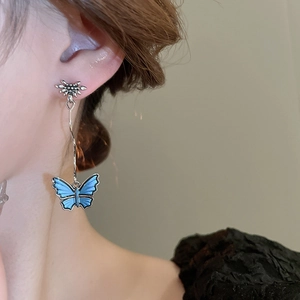 Close-up of model wearing blue butterfly drop earrings with silver flower studs