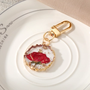 Detail of handmade resin keychain with real red dried flower and gold foil in gold frame