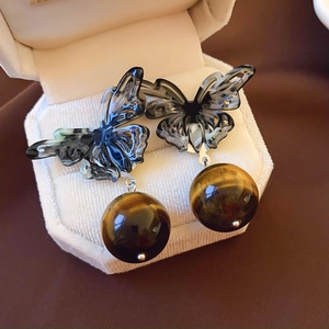 Detail view of brown tiger eye stone earrings with a grey butterfly design in a jewelry box