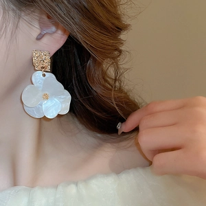 Close-up of model wearing gold square and white acrylic flower drop earrings with a pearl finish