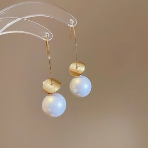 Close-up of gold sequin earrings with long hooks and white pearls on a minimalist stand