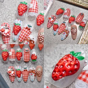 Macro detail of 3D strawberry charms and red gingham patterns on press-on nails