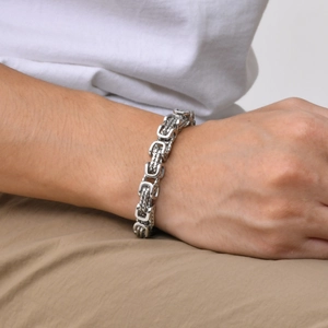 Close-up of a silver stainless steel Byzantine chain bracelet on a male wrist