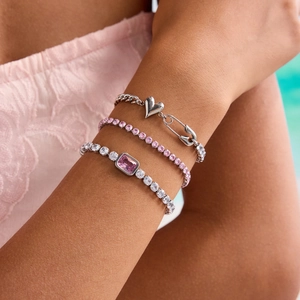 Close-up of stacked bracelets with pink gems and heart charm on woman's wrist