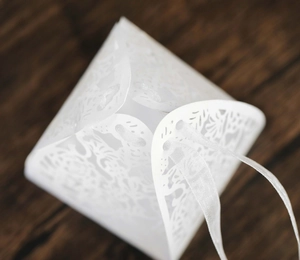 Close-up of white paper candy box with intricate hollow plant patterns and ribbon