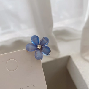 Detail of blue flower hair clip with pearl center and translucent petals on display card