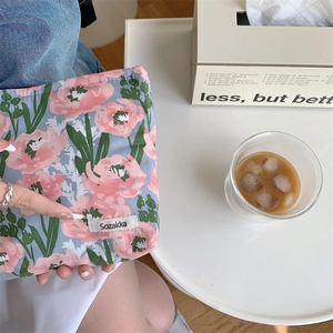 Detail of floral cotton makeup bag held by hand in a lifestyle setting with aesthetic props